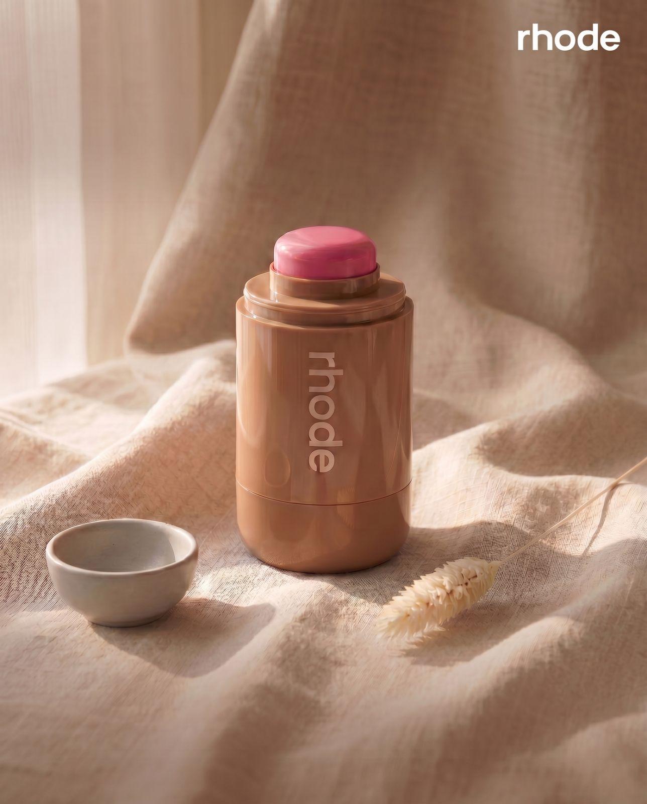 Editorial product shot — Rhode stick on draped linen with soft window light, dried wheat, ceramic bowl